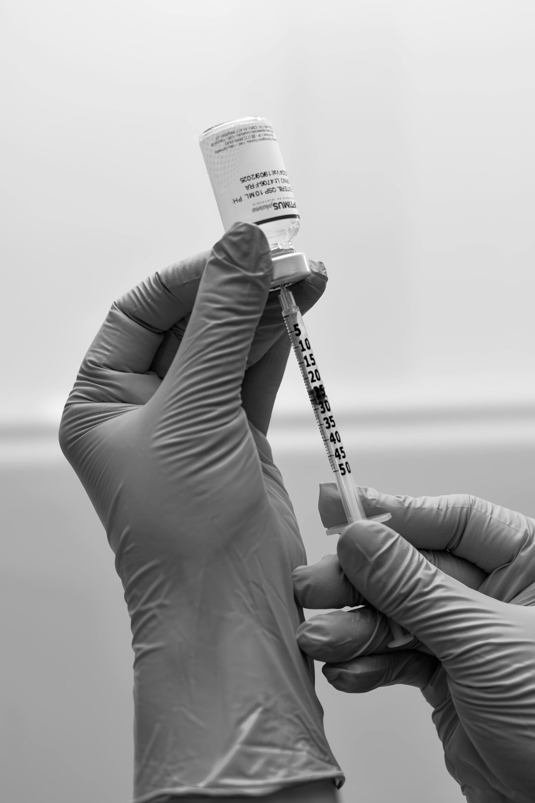 Close-up of a gloved person preparing a medical syringe in a clinical setting.